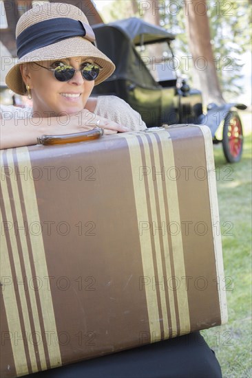 Pretty 1920s dressed girl with suitcase with room for text near vintage car and cabin