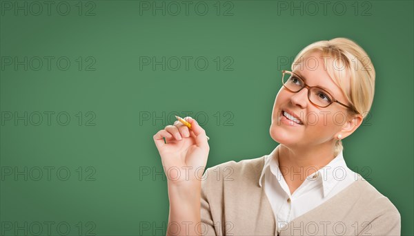 Attractive young woman with pencil and glasses in front of blank chalk board