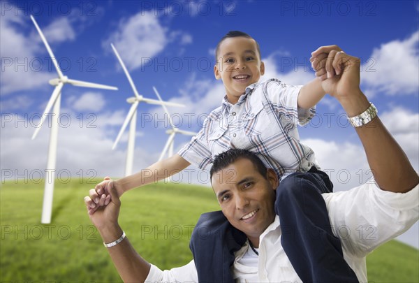 Happy hispanic father and son with wind turbine farm over blue sky