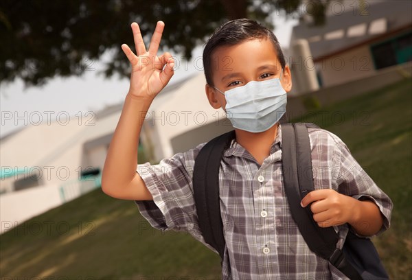 Hispanic student boy wearing face mask with backpack on school campus