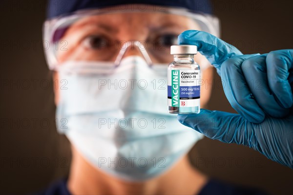 Female medical worker holding coronavirus vaccine vial wearing protective face mask and goggles