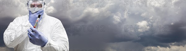 Male doctor or nurse in hazmat gear holding positive coronavirus test tube cloudy sky banner