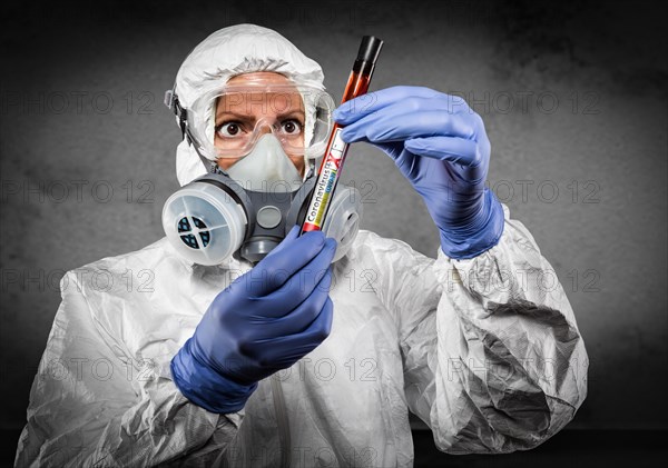 Female doctor or nurse in hazmat gear holding positive coronavirus test tube