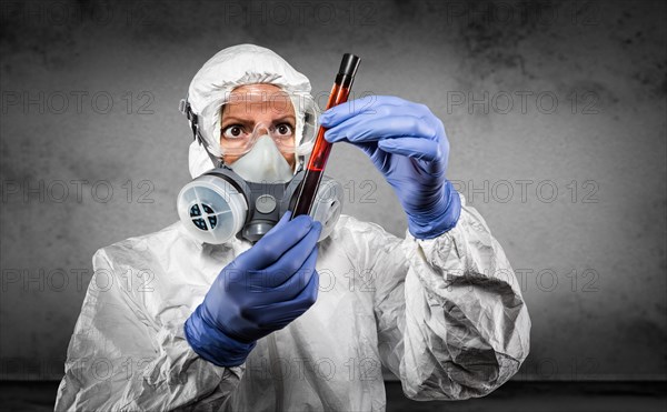 Woman in hazmat suit and gas mask holding test tube of blood in dark room