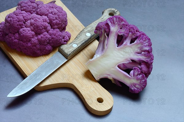 Halved purple cauliflower on wooden board with kitchen knife