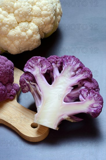 Halved purple cauliflower on wooden board with kitchen knife