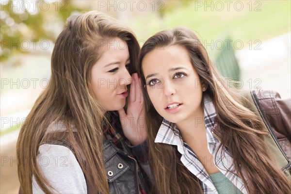 Two attractive mixed-race woman with backpacks whispering secrets outside