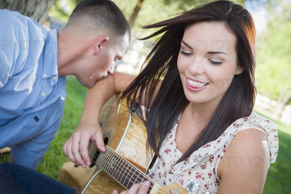 Happy mixed-race couple at the park playing guitar and singing songs