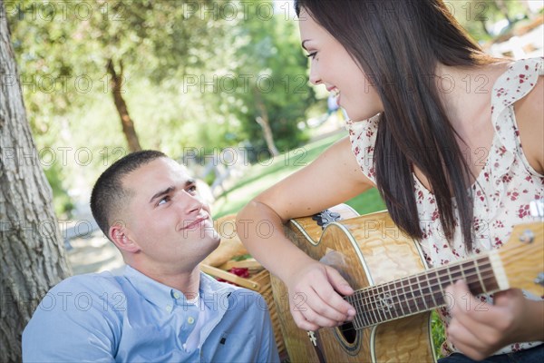 Happy mixed-race couple at the park playing guitar and singing songs