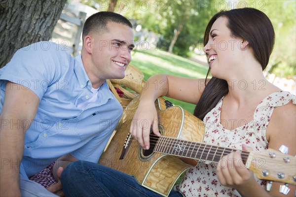 Happy mixed-race couple at the park playing guitar and singing songs