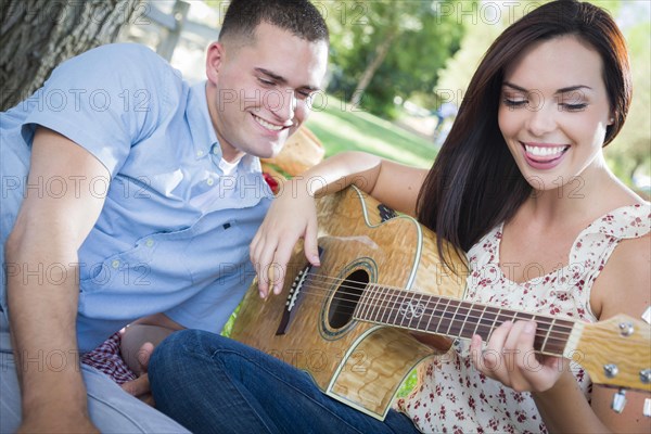 Happy mixed-race couple at the park playing guitar and singing songs