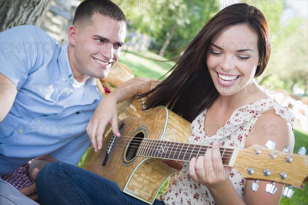 Happy mixed-race couple at the park playing guitar and singing songs