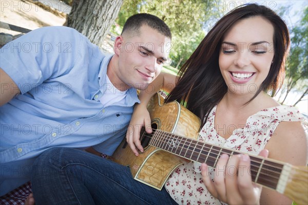 Happy mixed-race couple at the park playing guitar and singing songs