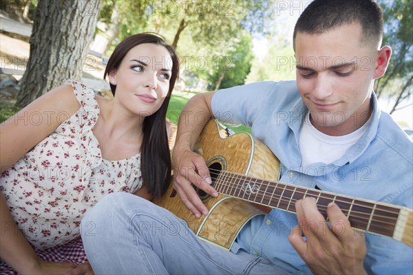 Happy mixed-race couple at the park playing guitar and singing songs