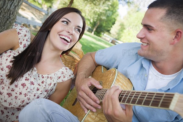 Happy mixed-race couple at the park playing guitar and singing songs