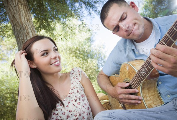 Happy mixed-race couple at the park playing guitar and singing songs