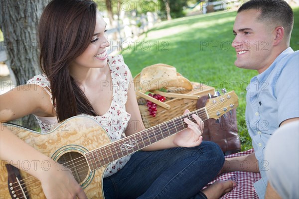 Happy mixed-race couple at the park playing guitar and singing songs