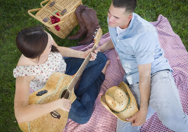 Happy mixed-race couple at the park playing guitar and singing songs