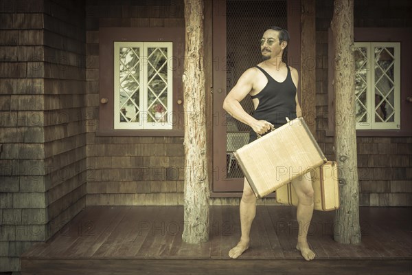 Goofy gentleman dressed in 1920's era swimsuit holding suitcases on porch of cabin