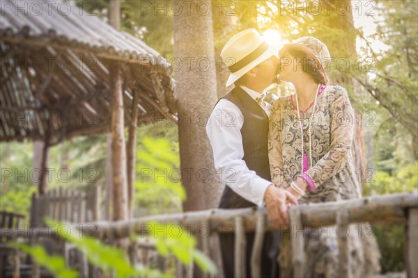 Attractive 1920s dressed romantic couple kissing on wooden bridge