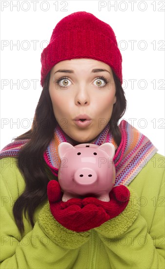 Expressive mixed-race woman wearing winter clothing holding piggybank isolated on white background