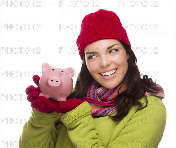 Happy mixed-race woman wearing winter clothing holding piggybank isolated on white background