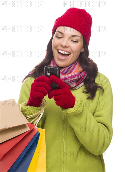 mixed-race woman wearing winter clothing holding shopping bags texting on cell phone isolated on white background