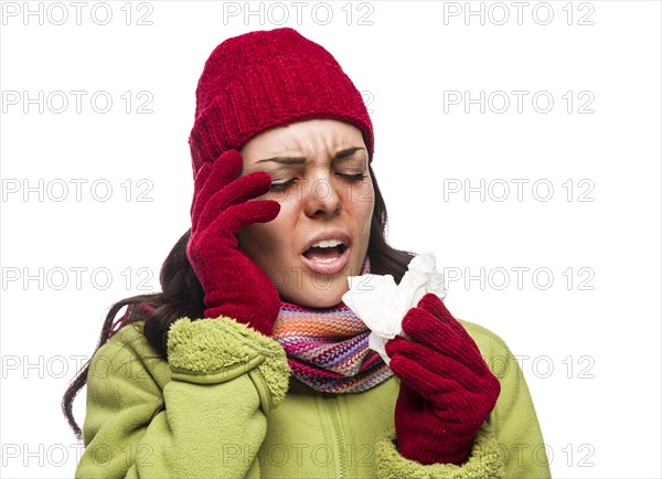 Sick mixed-race woman wearing winter hat and gloves blowing her sore nose with a tissue isolated on white background