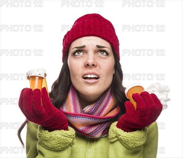 Sick mixed-race woman wearing winter hat and gloves with a tissue holding empty medicine bottle isolated on white