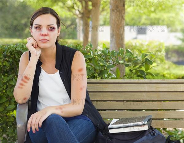 Sad bruised and battered young woman sitting on bench outside at a park