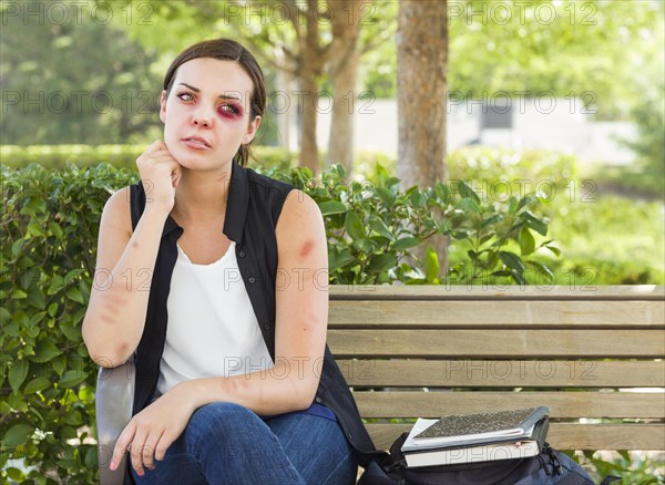 Sad bruised and battered young woman sitting on bench outside at a park