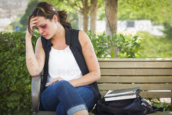 Sad bruised and battered young woman sitting on bench outside at a park