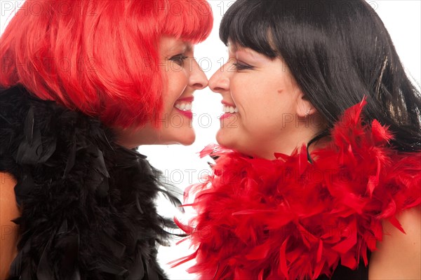 Red and black haired women with feather boas touching noses and smiling at each other