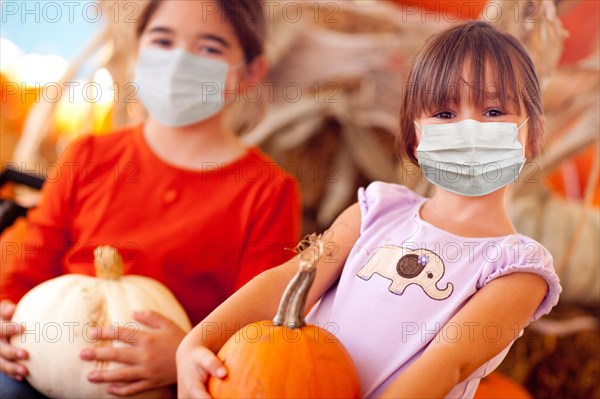 Cute little girls holding their pumpkins at A pumpkin patch wearing medical face masks