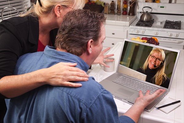 Couple in kitchen using laptop with customer support woman on the screen