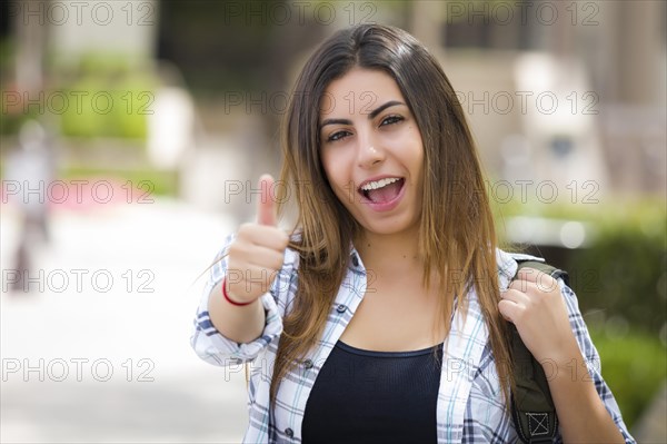 Attractive mixed race female student carrying backpack on school campus with thumbs up