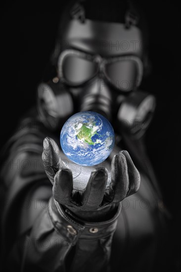 Menacing entity wearing fallout gas mask threatening planet earth with gloved hand