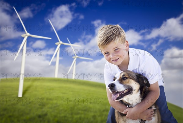 Handsome young blue eyed boy and dog playing near wind turbines and grass field