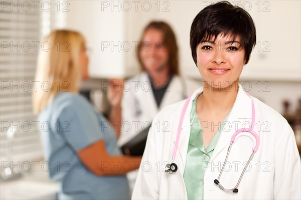 Pretty latino doctor smiles at the camera as colleagues talk behind her