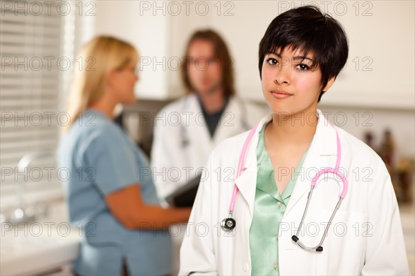 Pretty latino doctor smiles at the camera as colleagues talk behind her