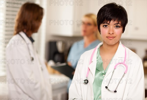 Pretty latino doctor smiles at the camera as colleagues talk behind her