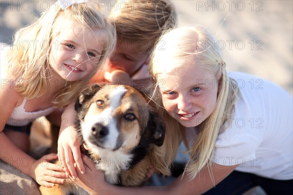 Cute sisters and brother playing with dog at the beach