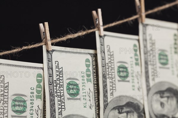 Hundred dollar bills hanging from a clothesline on a dark background