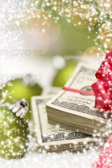 Stack of one hundred dollar bills with red bow near green christmas ornaments on snow flakes with snow flake border