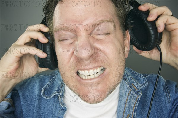 Shocked man desperately trying to take off his headphones
