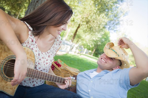 Happy attractive mixed-race couple with guitar and cowboy hat in the park