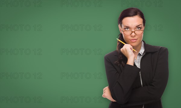 Serious young woman with pencil and glasses in front of blank chalk board