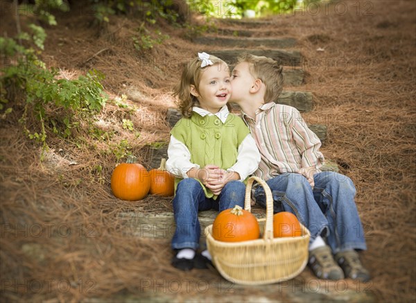 Adorable brother and sister children sitting on wood steps with pumpkins whispering secrets or kissing cheek