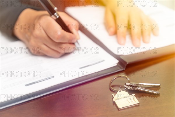 Woman signing real estate contract papers with house keys and home keychain in front