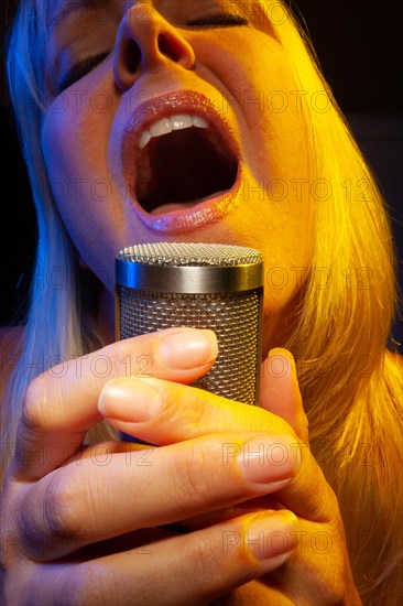 Female vocalist under gelled lighting sings with passion into condenser microphone